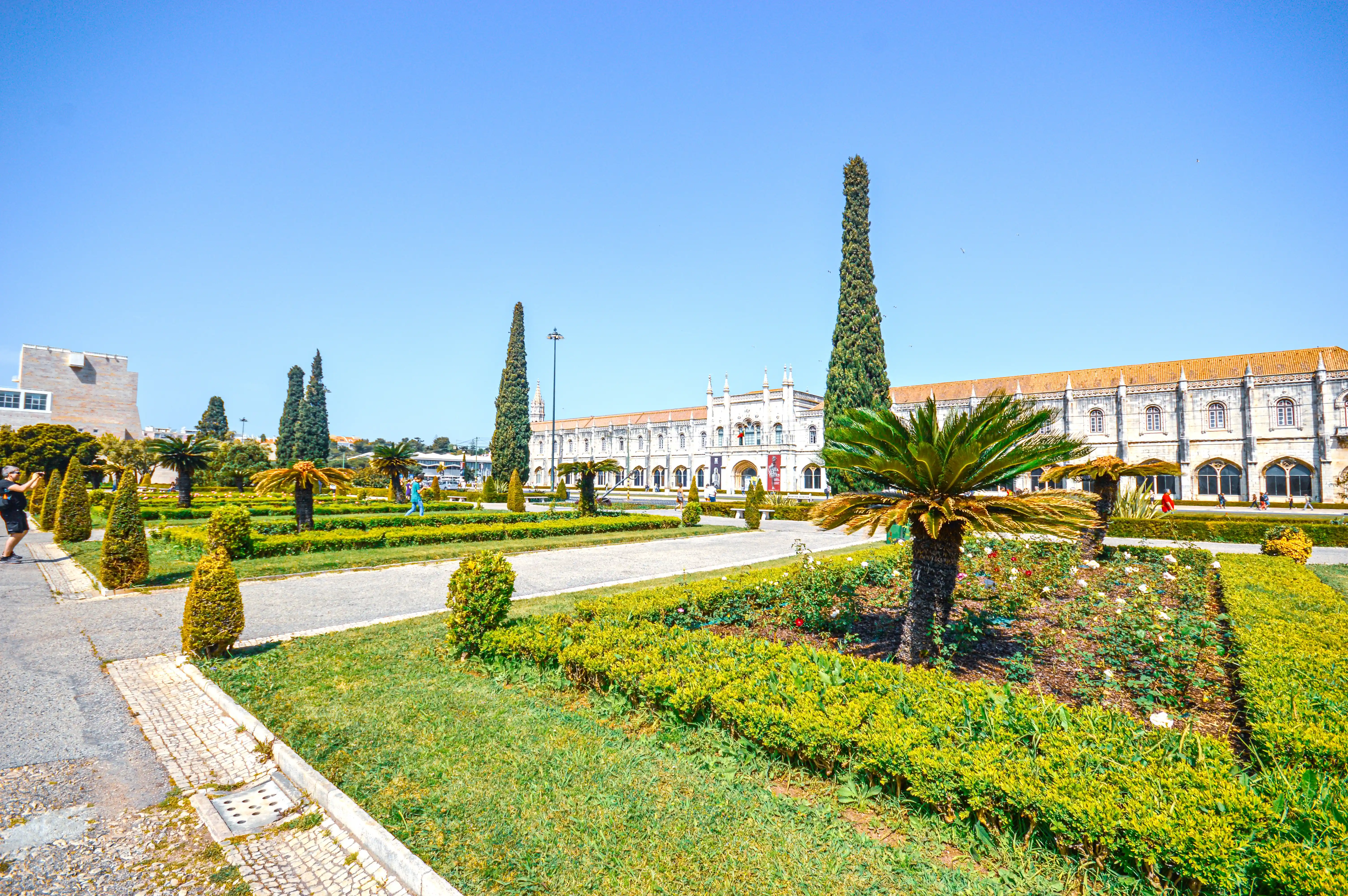 Jerónimos Monastery in Lisbon with manicured gardens and palm trees under a clear blue sky.